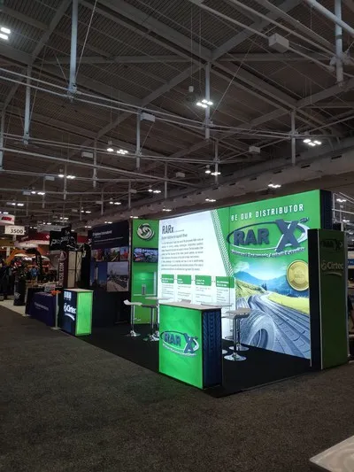 Moderno stand temático iluminado con pantallas LED y zona de atención tipo lounge para exhibición de asfalto y caucho.