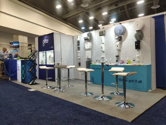 Stand de Glite con dispensadores de jabón y mesas en ferias comerciales en Estados Unidos dentro de un centro de expo